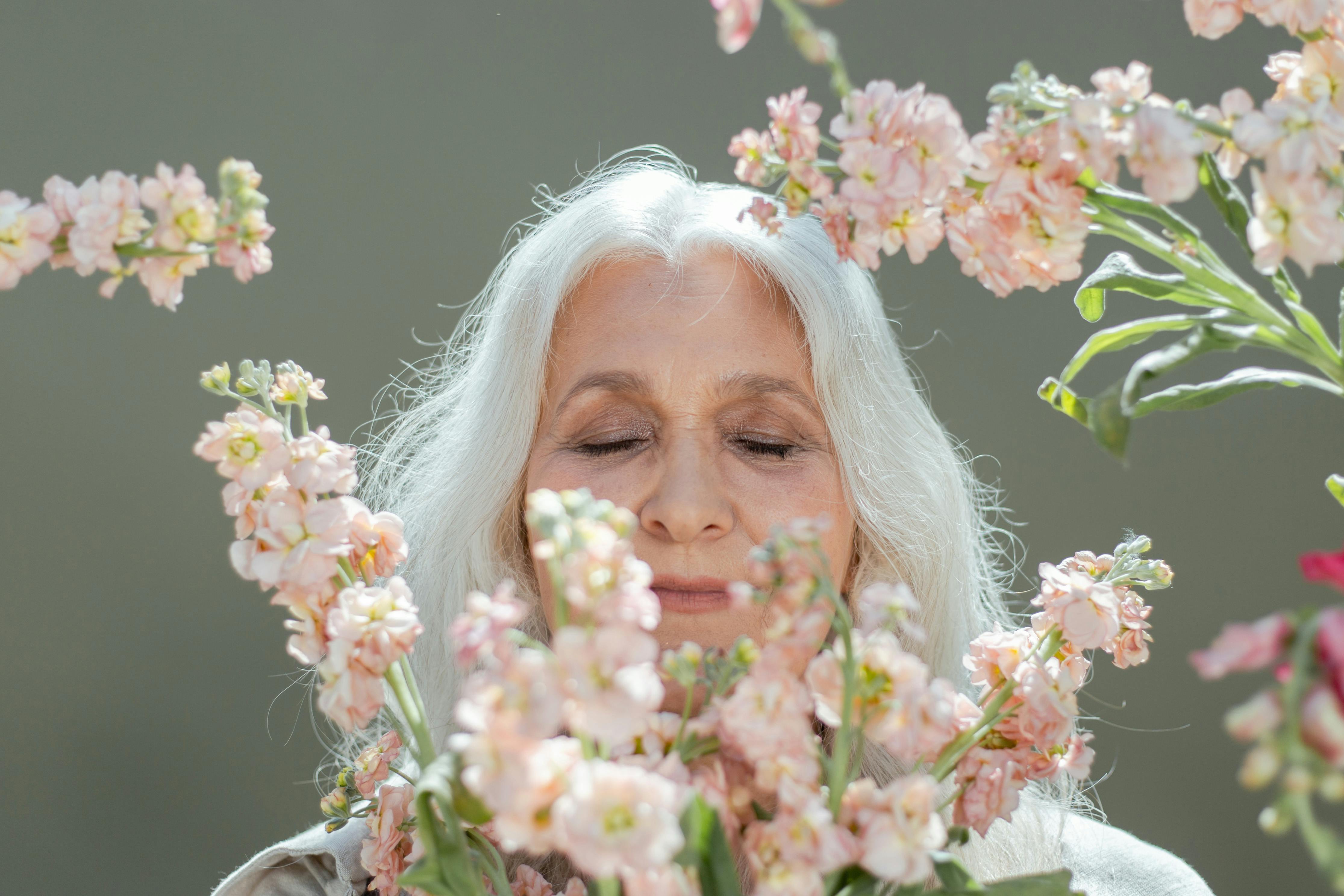 Woman with white hair, surrounded by light pink flowers